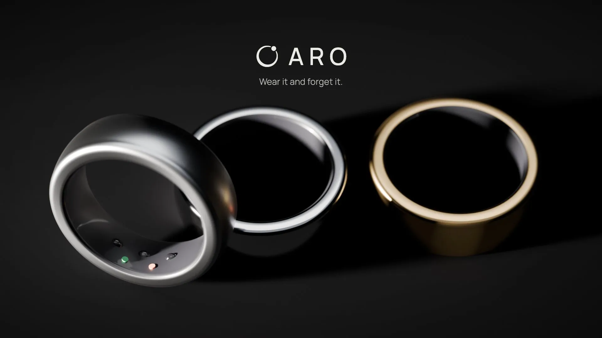 Three smart rings in titanium, silver, and gold on a black surface under a hard raking light