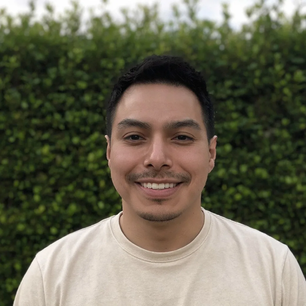 Jake Reátegui, smiling, in front of a green hedge