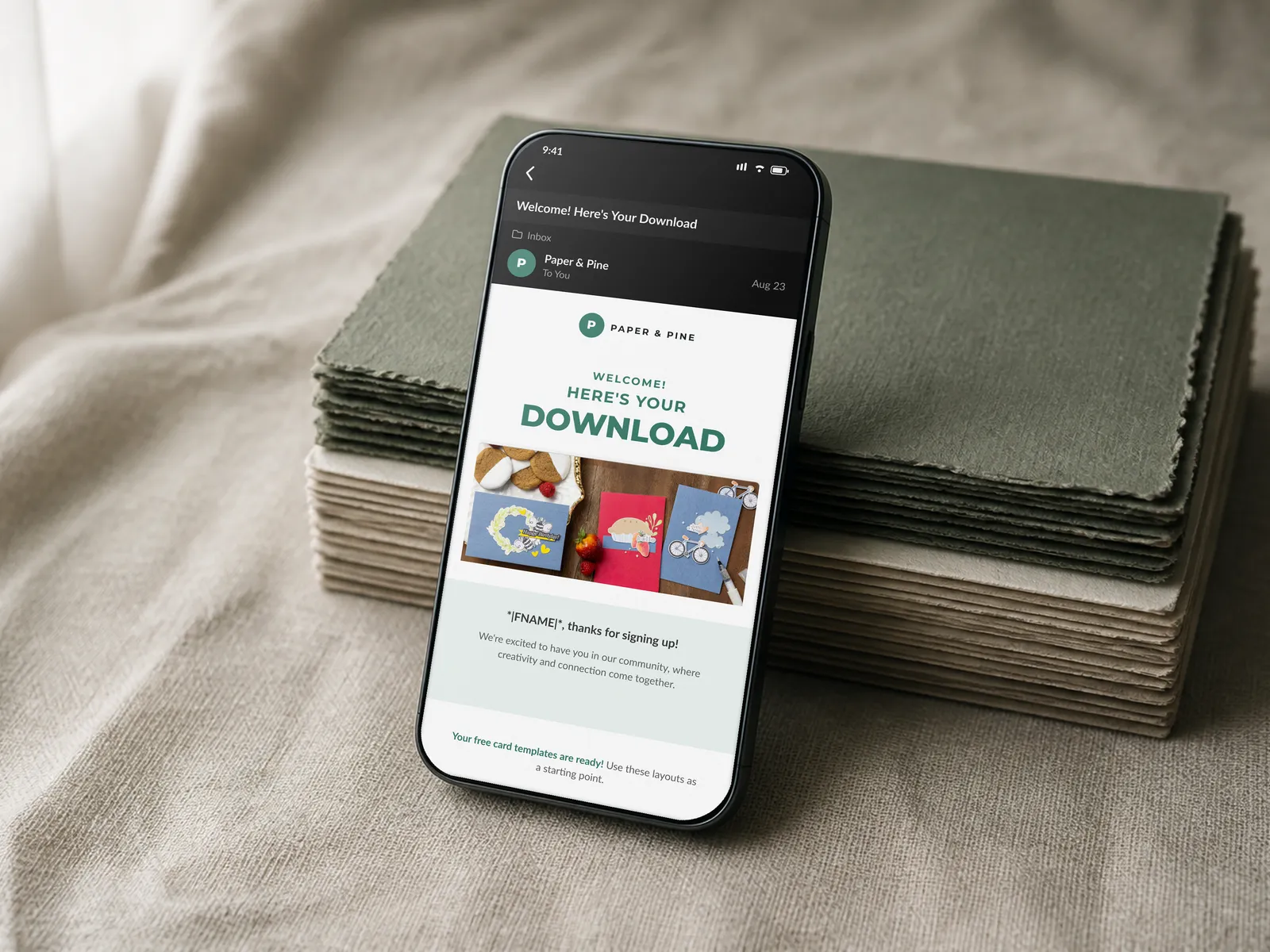 Email 1 welcome message with its free template download offer, shown on a phone propped against a stack of craft cardstock