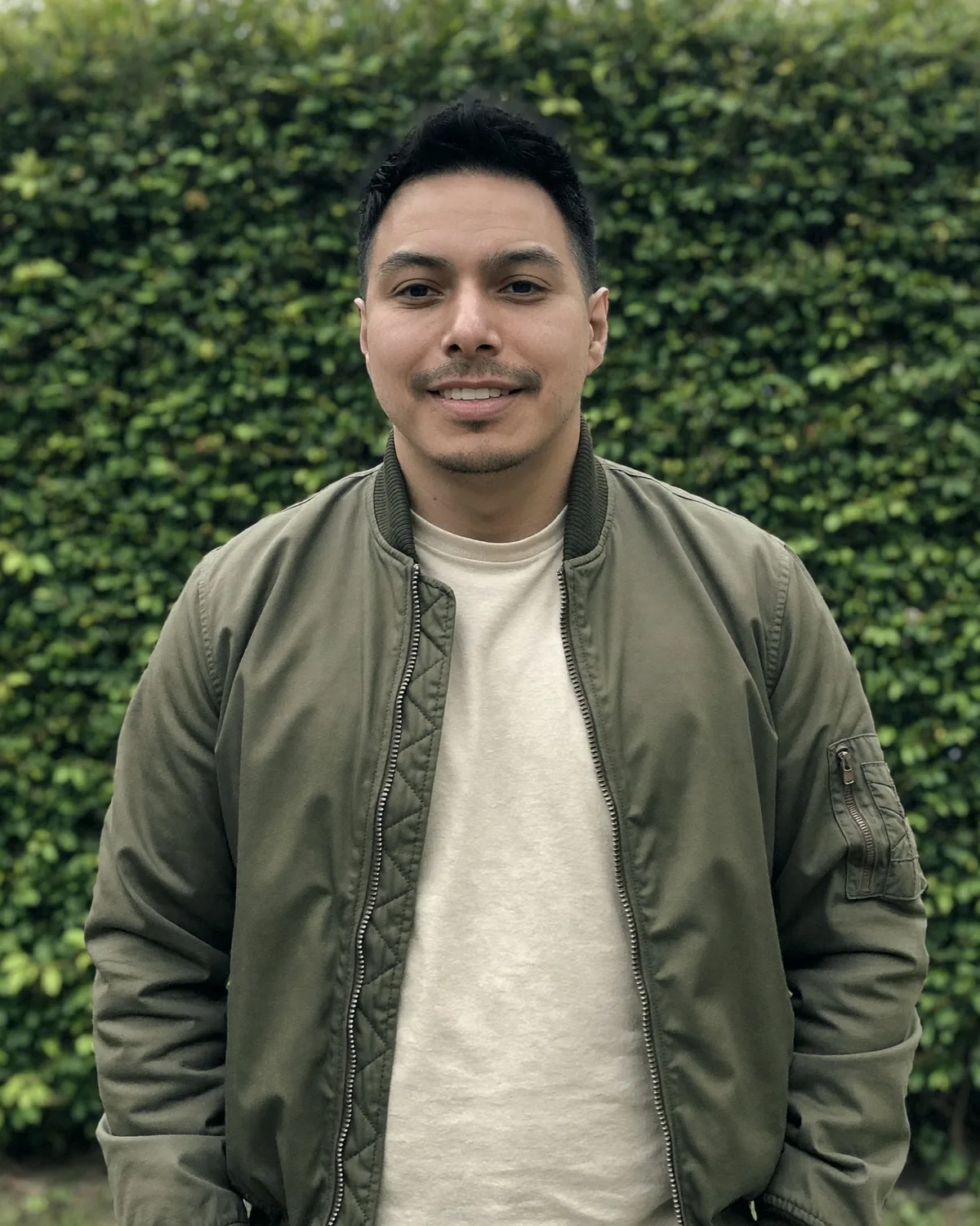 Jake Reátegui, standing outdoors in front of a green hedge